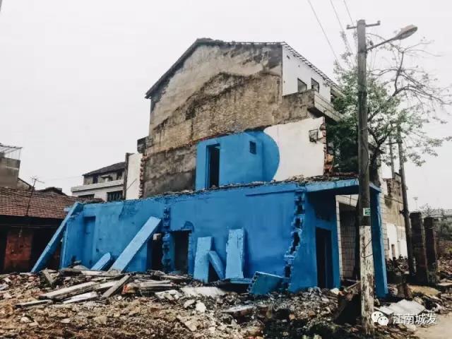 △ 這棟建筑是臨江最近的半拆遷建筑物的遺留，沅江和堤壩成為了展覽的天然背景。創(chuàng)作團(tuán)隊(duì)對這棟建筑進(jìn)行了半涂裝，將符號性的沅水曲線與拆遷進(jìn)行中的建筑立面進(jìn)行意義的疊造，它們共同觸發(fā)了場所空間多元語境的生成，把拆遷這種暫時(shí)破壞性、干擾性的介入行動與沅水右岸發(fā)展的未來性、美好性緊密融合。
